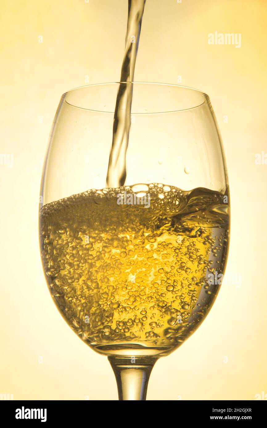 Ein Glas gefüllt mit Weißwein auf goldenem Hintergrund Stockfoto