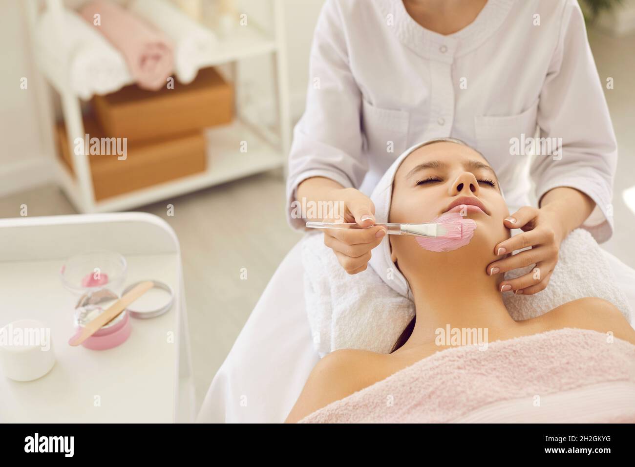 Entspannte junge Frau genießt kosmetische rosa Ton Gesichtsmaske im Beauty-oder Spa-Salon Stockfoto