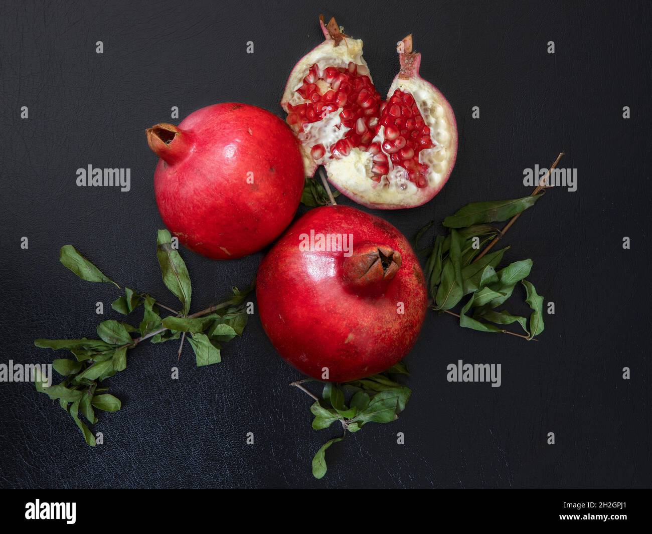 Granatapfelfrüchte mit Zweigen auf schwarzem Hintergrund isoliert Stockfoto