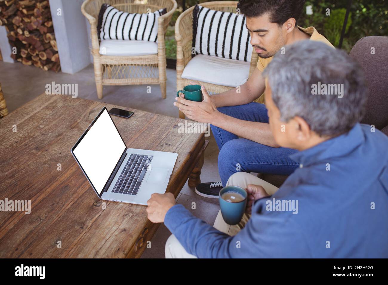 Sohn und älterer Vater mit birazialen Erwachsenen halten Tassen Kaffee und führen einen Videoanruf mit dem Laptop durch Stockfoto