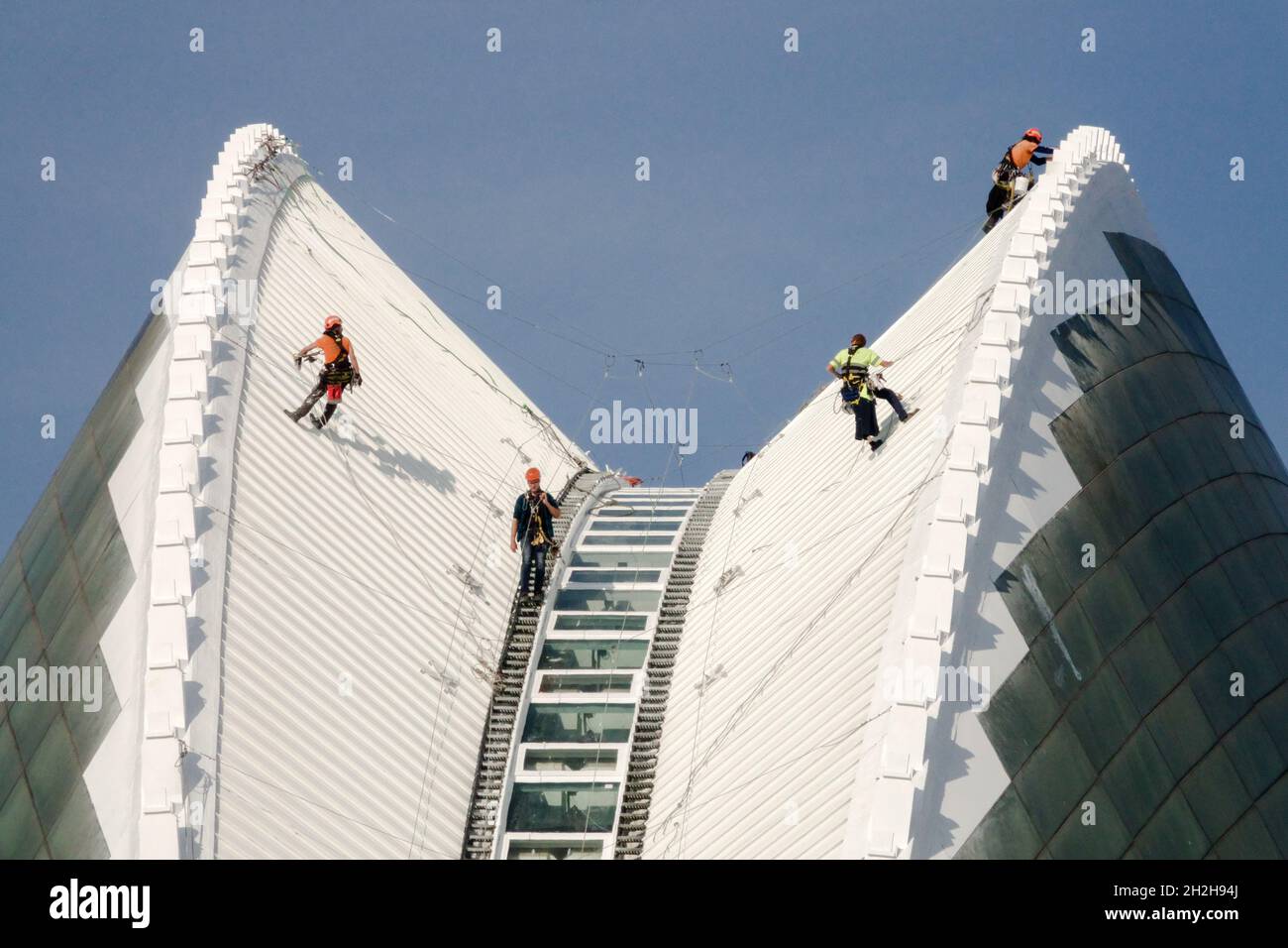Eine Gruppe von Arbeitern, die an Kletterseilen hängen, kontrolliert das moderne Gebäude in Valencia, der Stadt der Künste und Wissenschaften Stockfoto