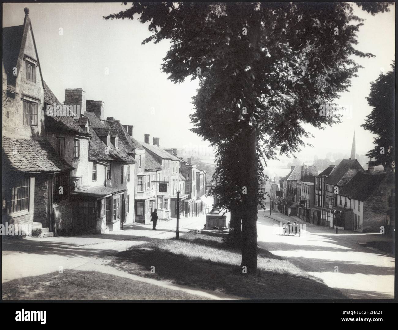 High Street, Burford, West Oxfordshire, Oxfordshire, 1925-1935. Der Blick nach Norden auf die High Street mit dem war Memorial im Vordergrund, das teilweise von Bäumen auf der Westseite der Fahrbahn verdeckt wird. Stockfoto