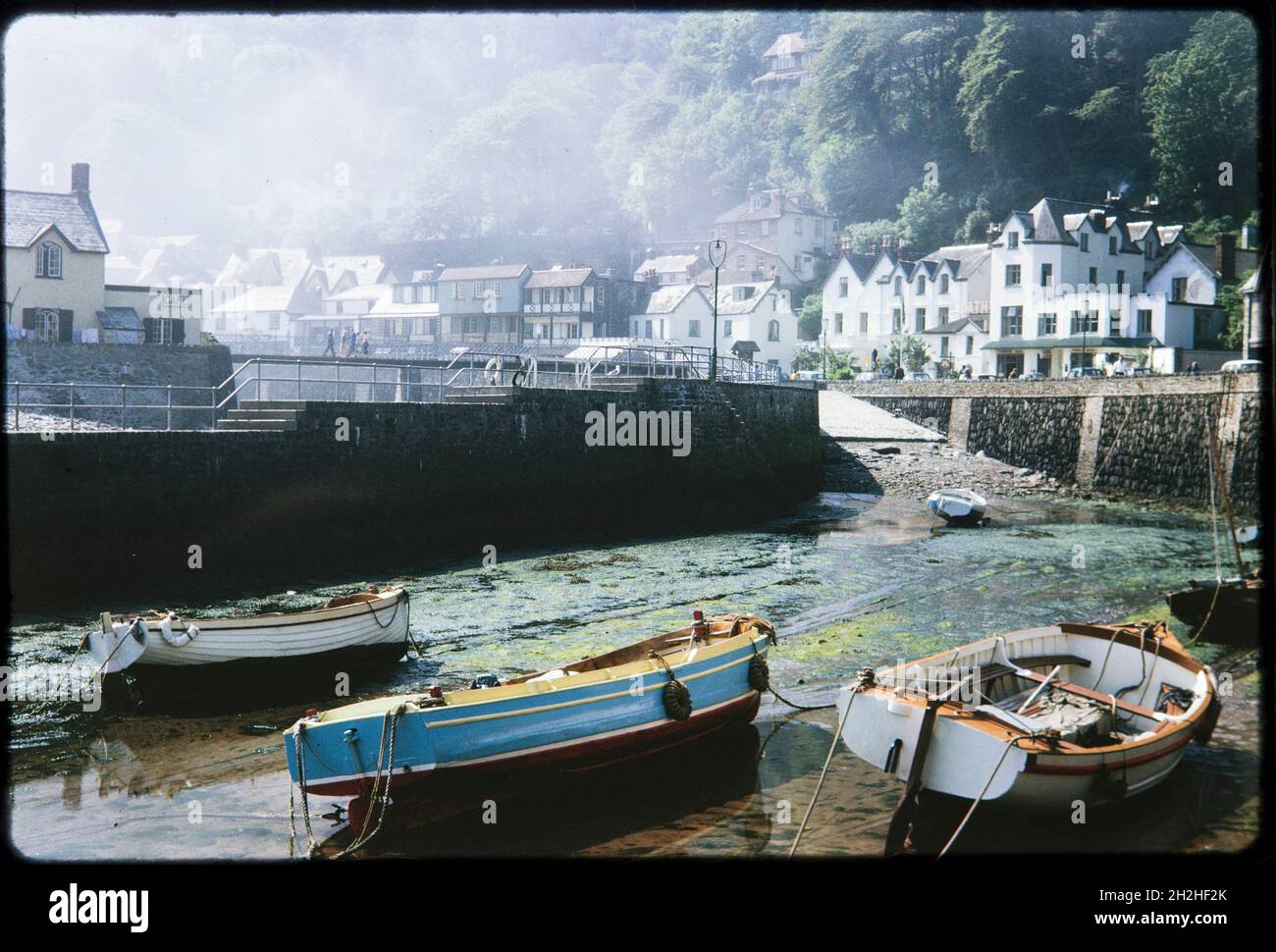 Lynmouth Harbor, Lynmouth, Lynton und Lynmouth, North Devon, Devon, 1963. Ein Blick über die Boote in Lynmouth Harbour bei Ebbe, mit Sonnenlicht, das auf Nebel über den Häusern an der Riverside Road und Lynmouth Street fällt. Stockfoto