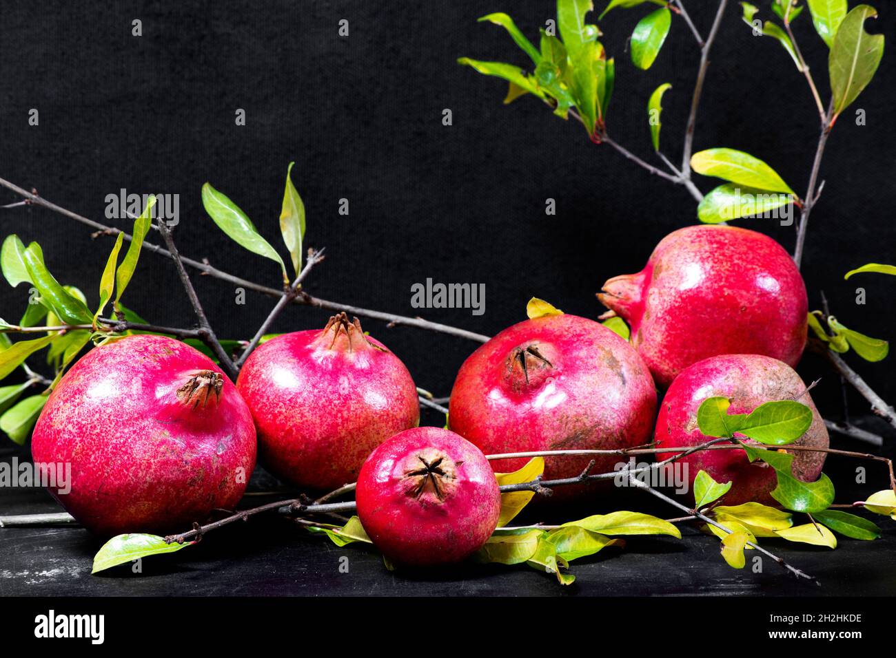 Rote Granatäpfel mit grünen Blättern auf altem Holzschneidebrett, Seitenansicht, dunkler Hintergrund Stockfoto