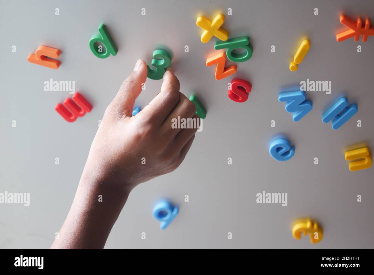 Kleiner Junge, der bunte Plastikbriefe auf einem Kühlschrank organisiert Stockfoto