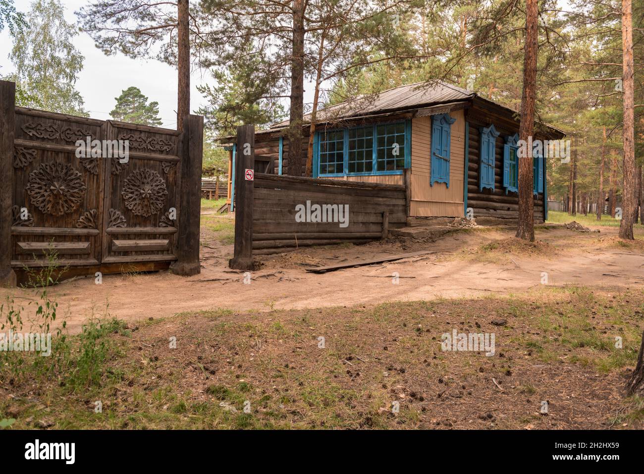 Ein traditionelles Holzhaus mit geschnitztem Zaun zwischen den Bäumen im Ethnographischen Museum in der Nähe von Ulan-Ude. Republik Burjatien, Russland Stockfoto