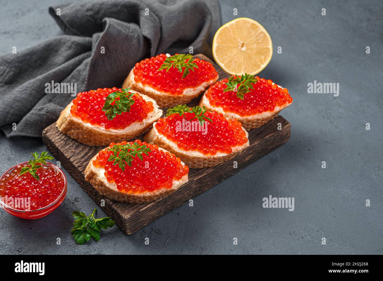 Sandwiches mit rotem Kaviar, Butter und Zitrone auf dunklem Grund. Seitenansicht, Kopierbereich. Stockfoto