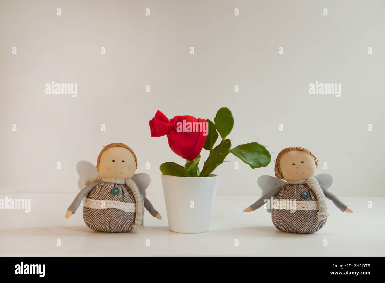 Grüner Kaktus mit rotem weihnachtshut oder Haube in weißem Topf mit weihnachtlichen lustigen Dekorationen. Heimpflanze Stockfoto
