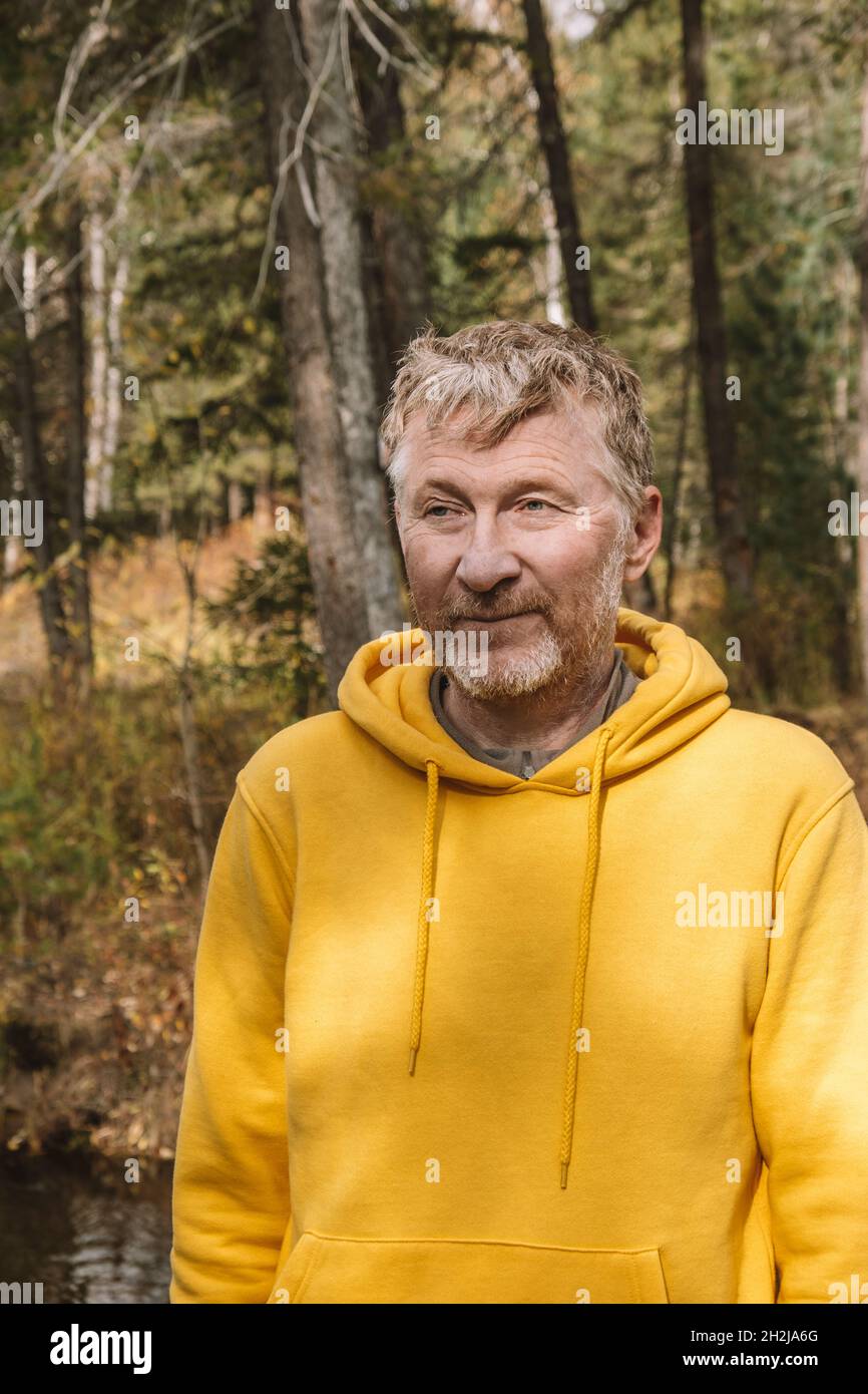 Ein authentisches Porträt eines lächelnden, unrasierten Mannes mittleren Alters mit gelbem Hoodie auf einem Spaziergang im Park. Ein hübscher Erwachsener. Nahaufnahme. Nachhaltige Umwelt. Stockfoto