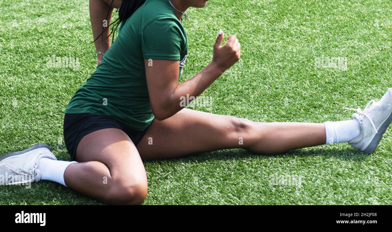 Nahaufnahme einer Sportlerin, die sich in einer Hürdenstrecke auf einem grünen Rasenfeld dehnt. Stockfoto
