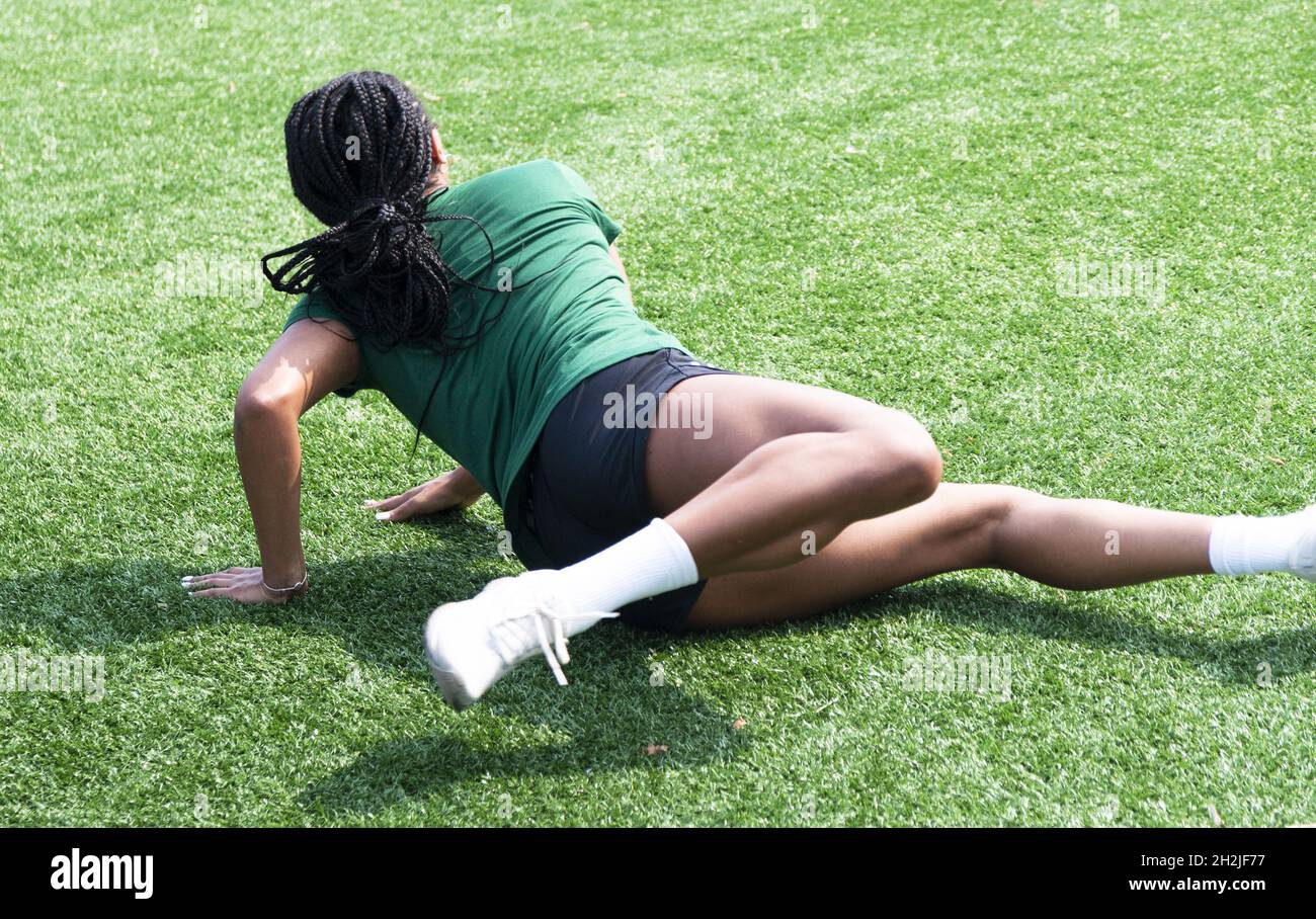 Eine athletische Frau, die sich auf einem grünen Rasenplatz ausdehnt. Stockfoto