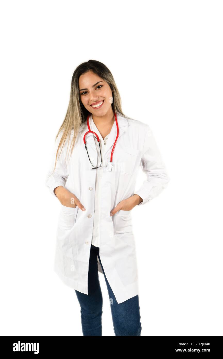 Junge Ärztin mit einem großen Lächeln, die mit ihren Händen in ihren Taschen auf weißem Hintergrund steht. Konzept der professionellen Frau, Gesundheitspersonal. Amerikanische Pl Stockfoto