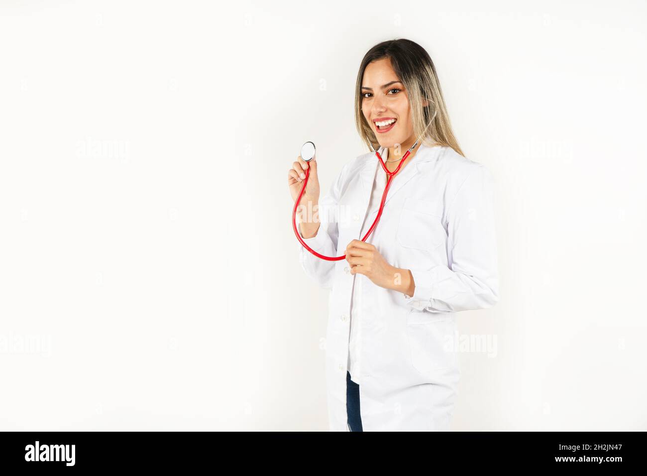 Junge lächelnde Ärztin aus Latina, die mit dem Stethoskop in den Händen steht und an ihrem Hals hängt. Konzept der professionellen Frau, Gesundheitspersonal. Mittel Stockfoto