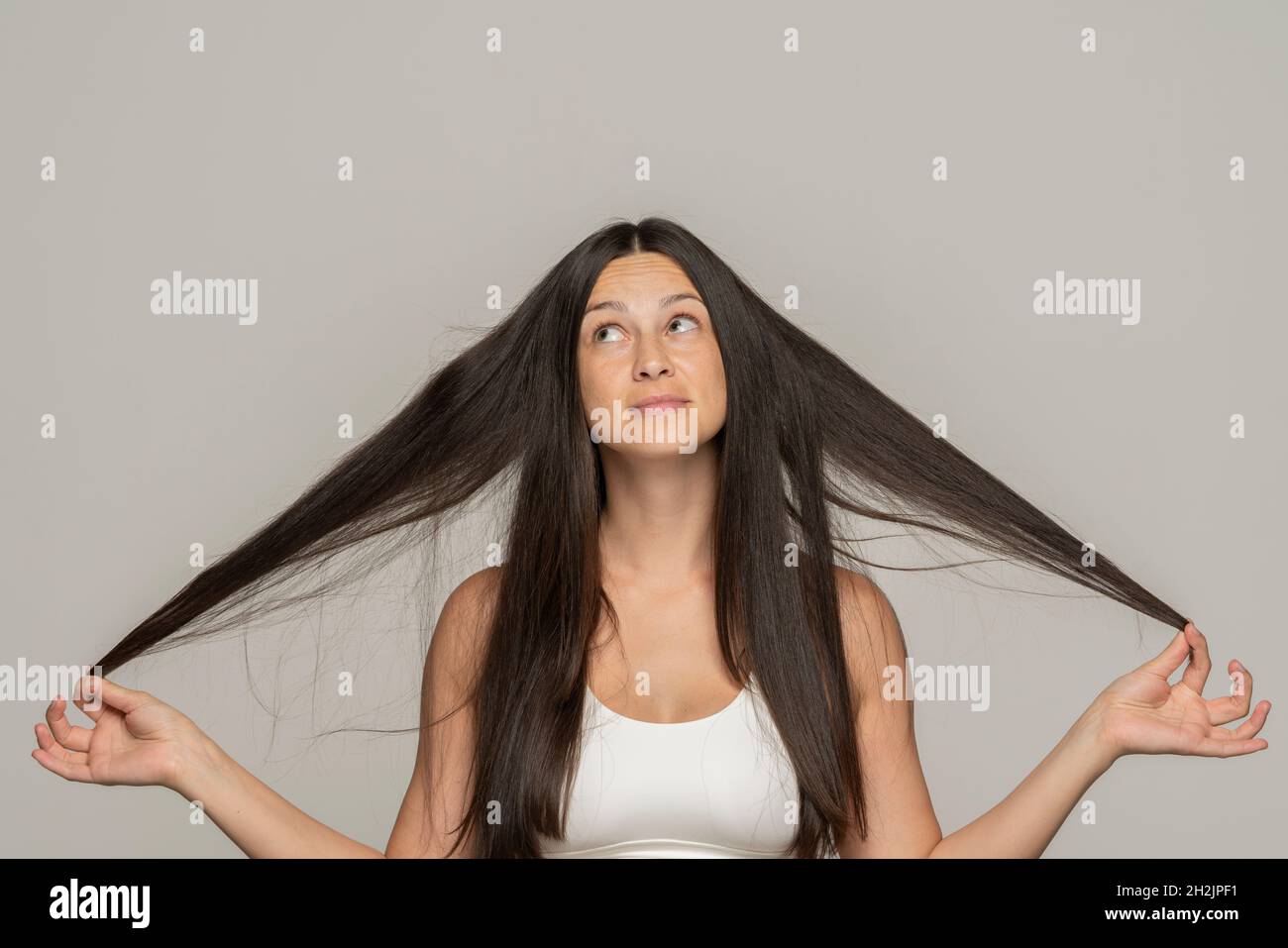 Eine junge Frau hält und zeigt ihr langes Haar auf grauem Hintergrund Stockfoto