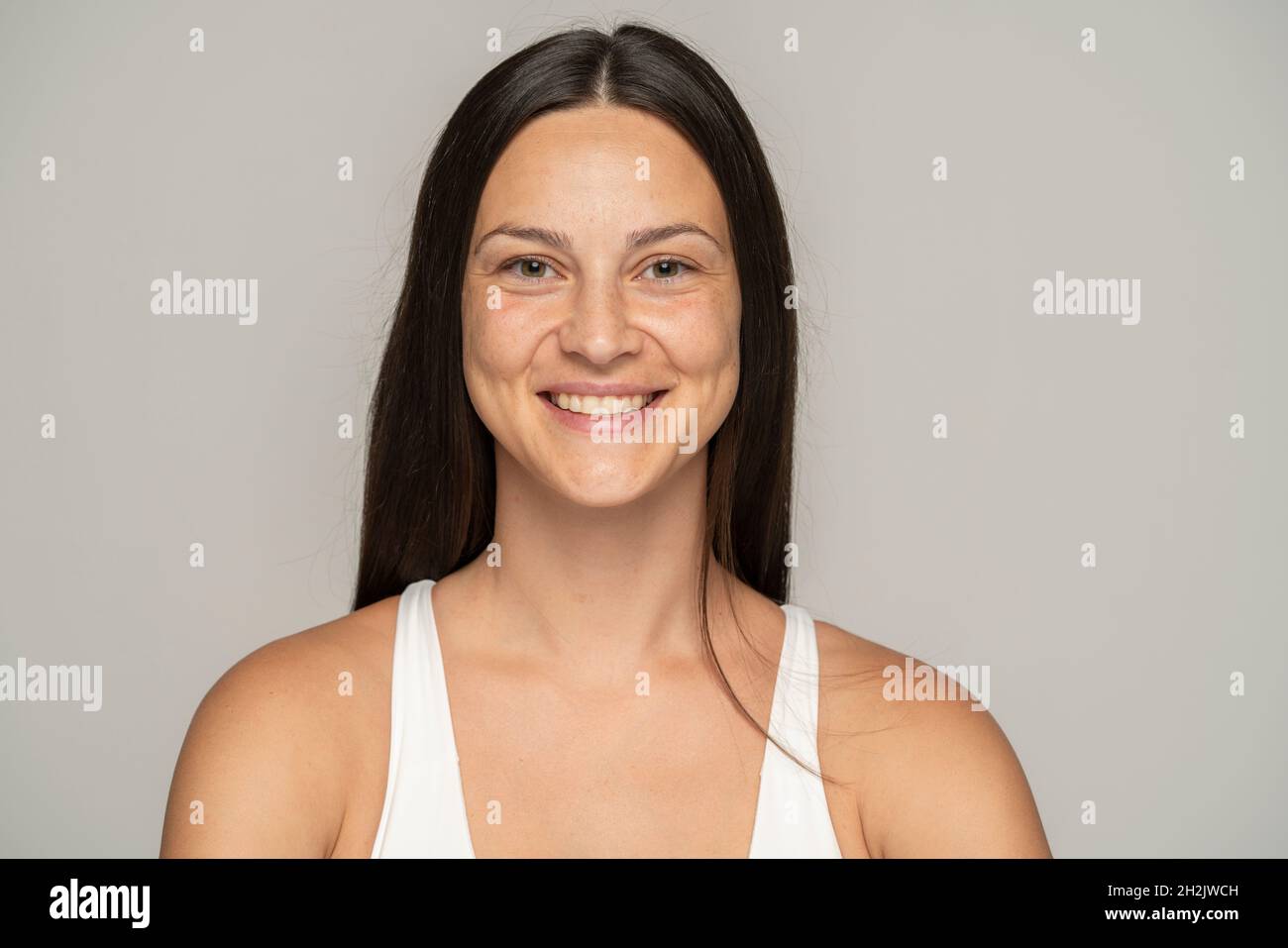 Eine junge lächelnde Frau ohne Make-up mit langen Haaren auf grauem Hintergrund Stockfoto