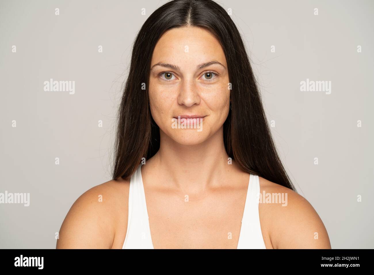Eine junge lächelnde Frau ohne Make-up mit langen Haaren auf grauem Hintergrund Stockfoto