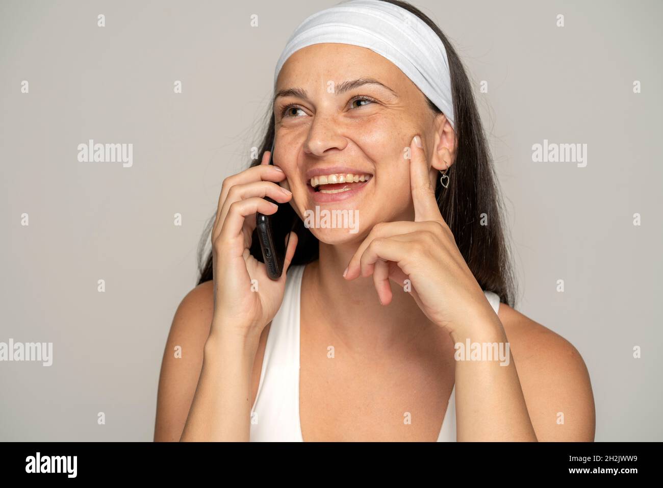Junge lächelnde Frau ohne Make-up mit Stirnband am Telefon auf einem grauen Hintergrund sprechen Stockfoto