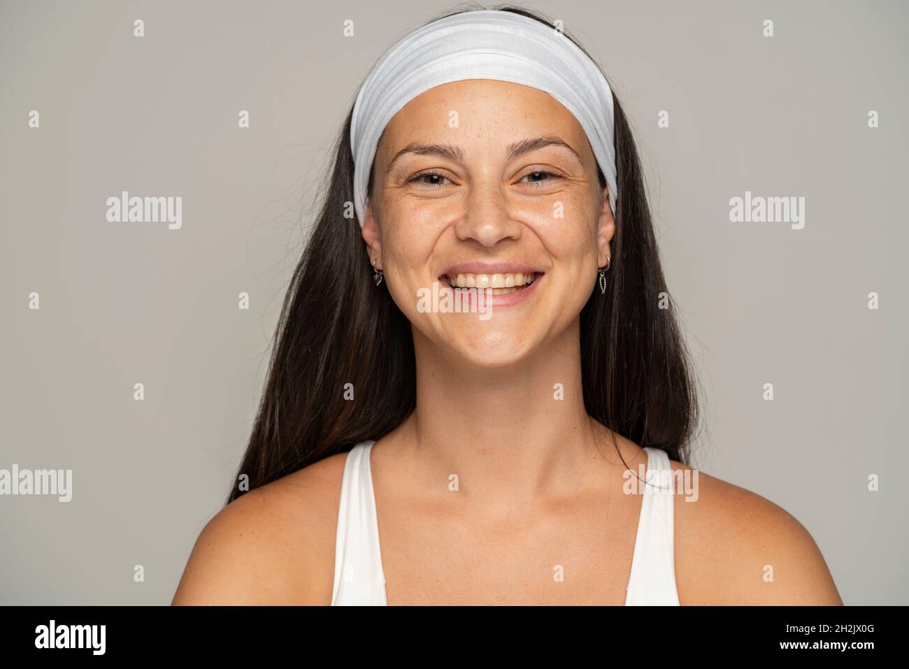 Porträt einer jungen glücklichen Frau ohne Make-up und Stirnband auf grauem Hintergrund Stockfoto