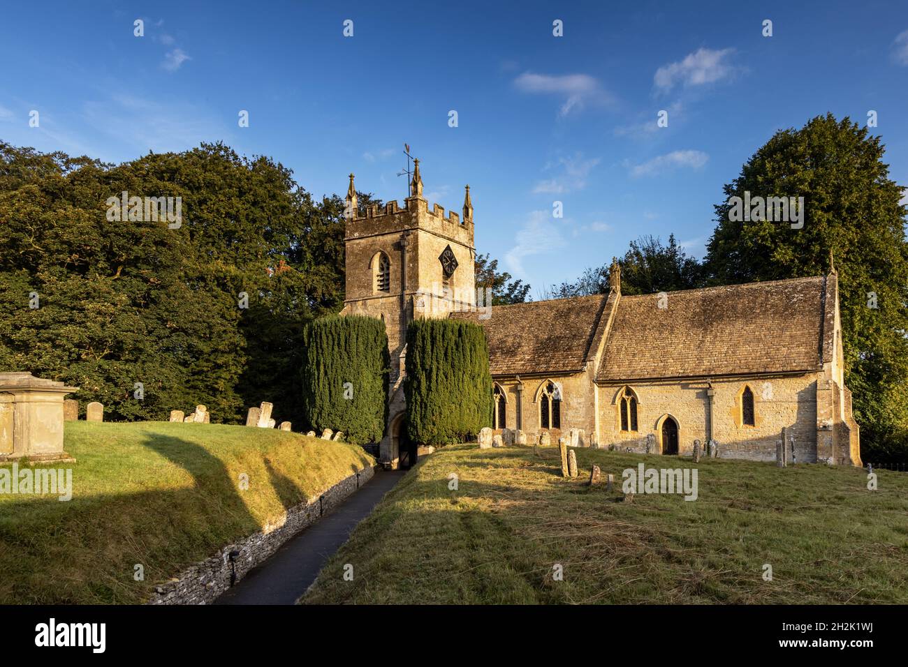 Die Morgensonne erleuchtet die wunderschöne St. Peter's Kirche im malerischen Cotswold Dorf Upper Slaughter in Gloucestershire, England. Stockfoto
