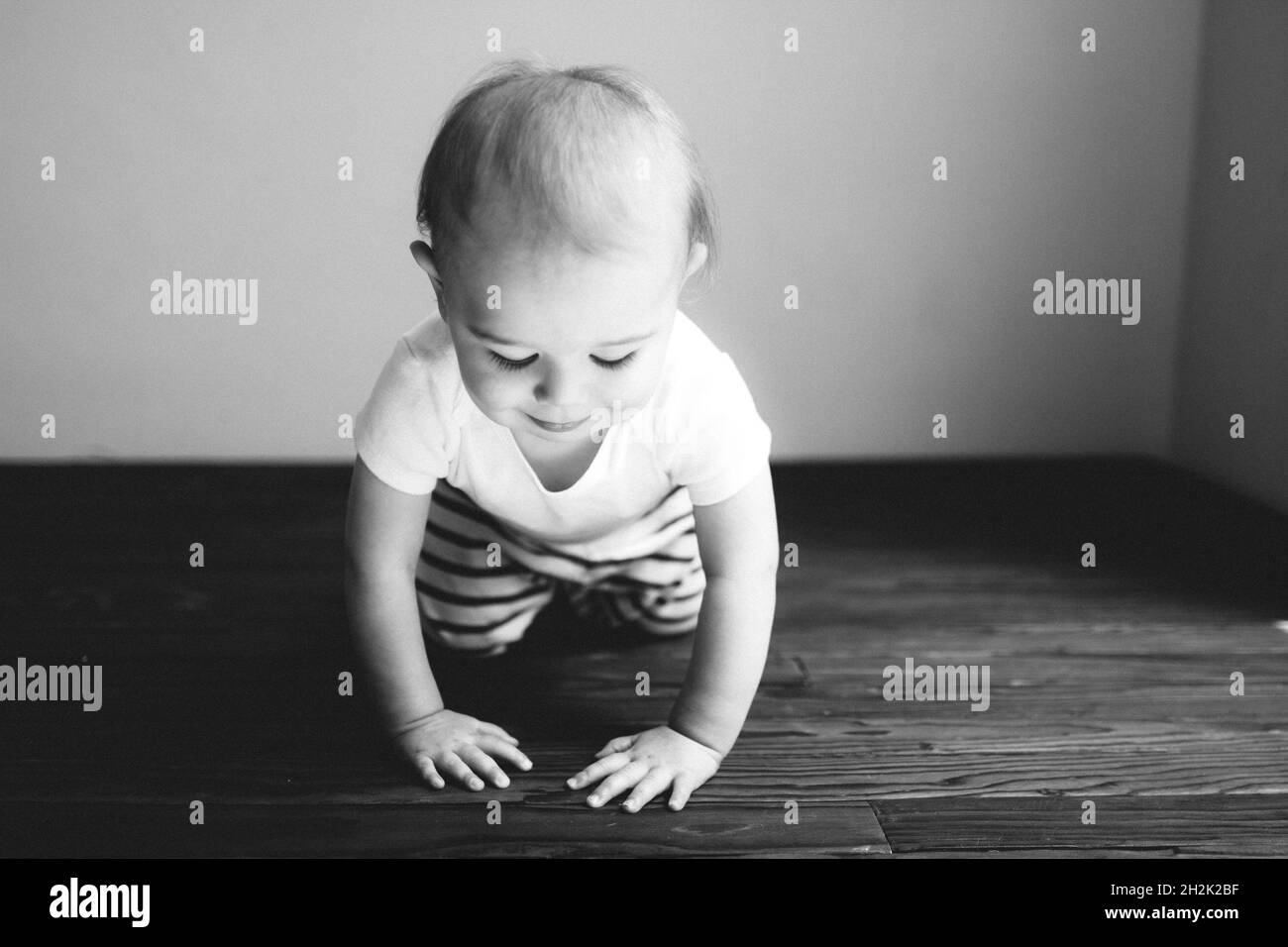 Schwarzweiß-Foto eines kleinen Jungen, der auf einem Holzboden kriecht Stockfoto