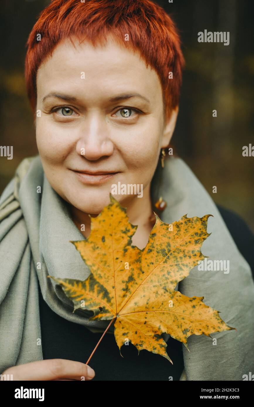 Eine Frau mittleren Alters von 30-40 Jahren mit einem herbstlichen Ahornblatt in der Hand. Nahaufnahme mit positivem Porträt, weibliche junge Erwachsene Stockfoto