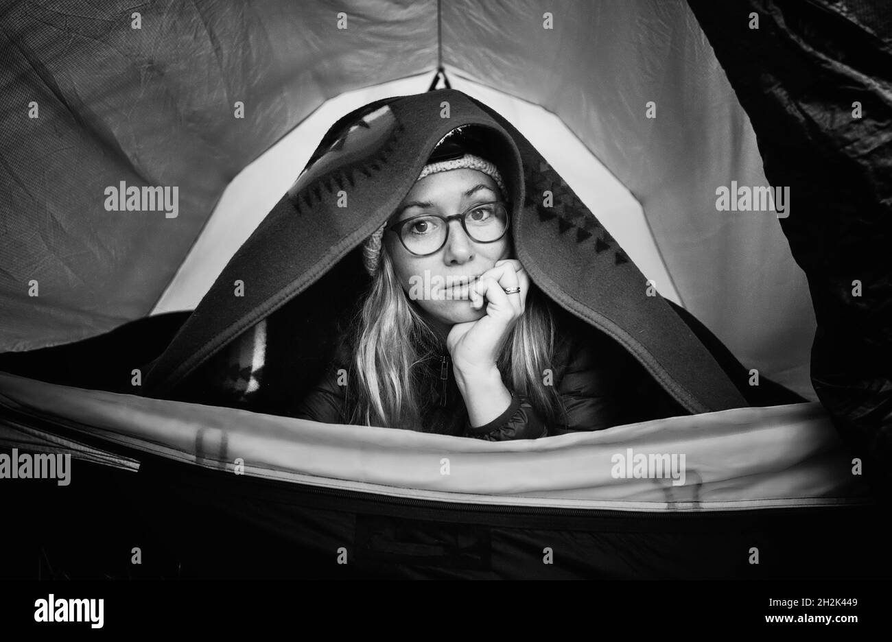 Porträt einer Frau, die sich im Zelt während des Alleincampens warm hält Stockfoto