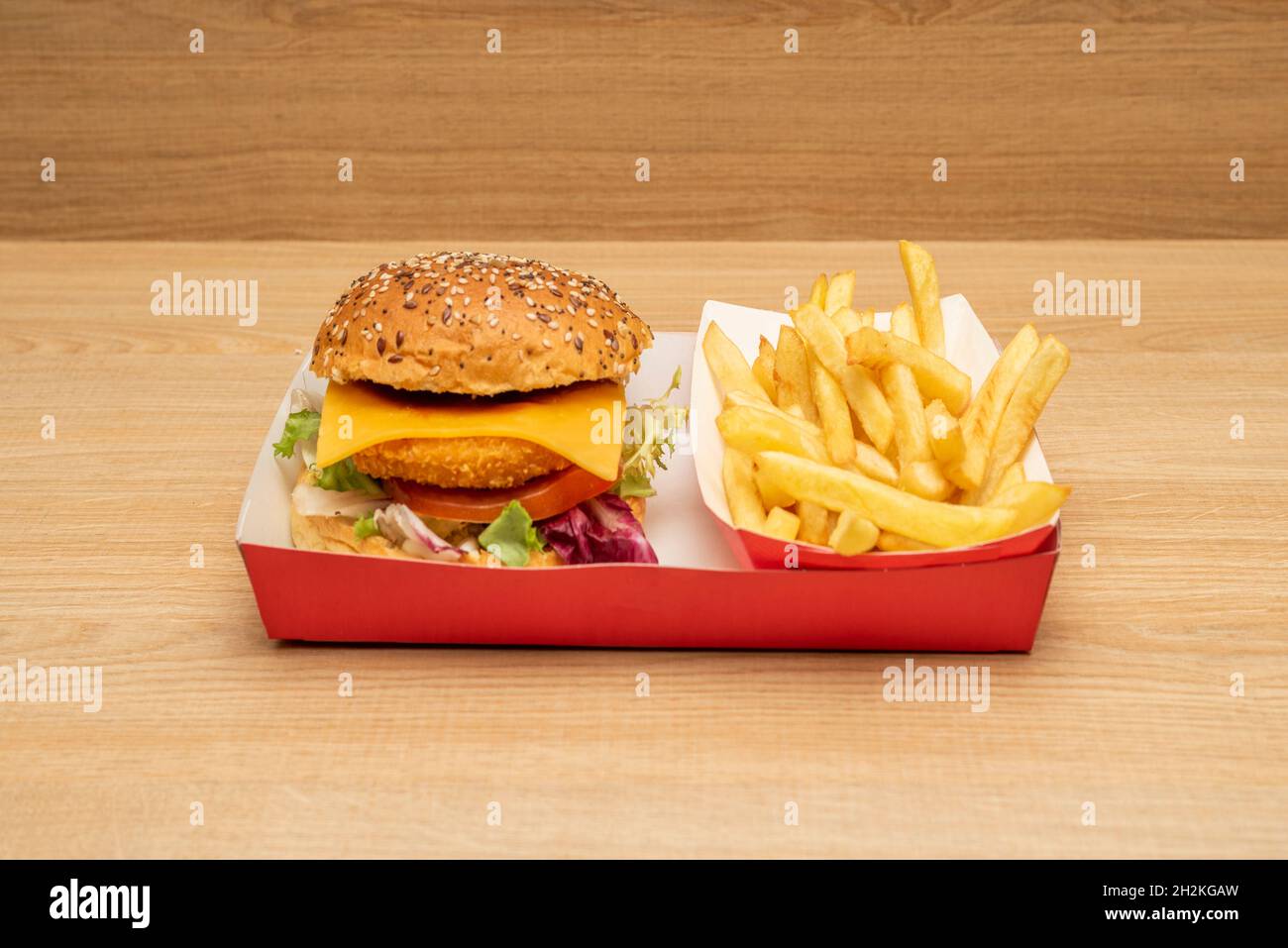 Knuspriger Chicken Burger mit Cheddar-Käse, Tomaten und Salat, Mayonnaise und Ketchup, Pommes auf einer hellen Holztheke Stockfoto