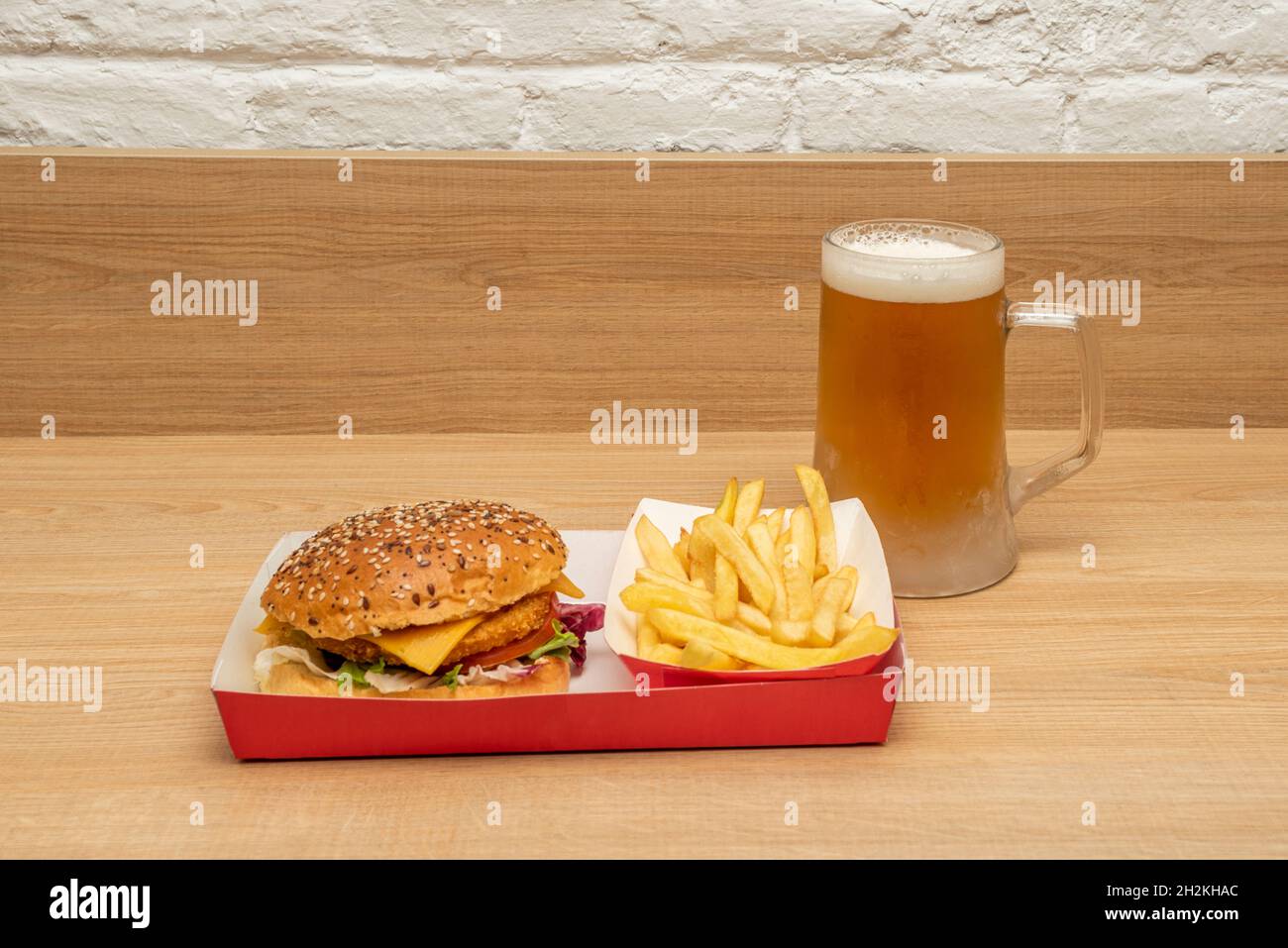 Knuspriger Chicken Burger mit Cheddar-Käse, Tomaten und Salat, Mayonnaise und Ketchup, Pommes Frites und eiskaltem Bierkrug Stockfoto