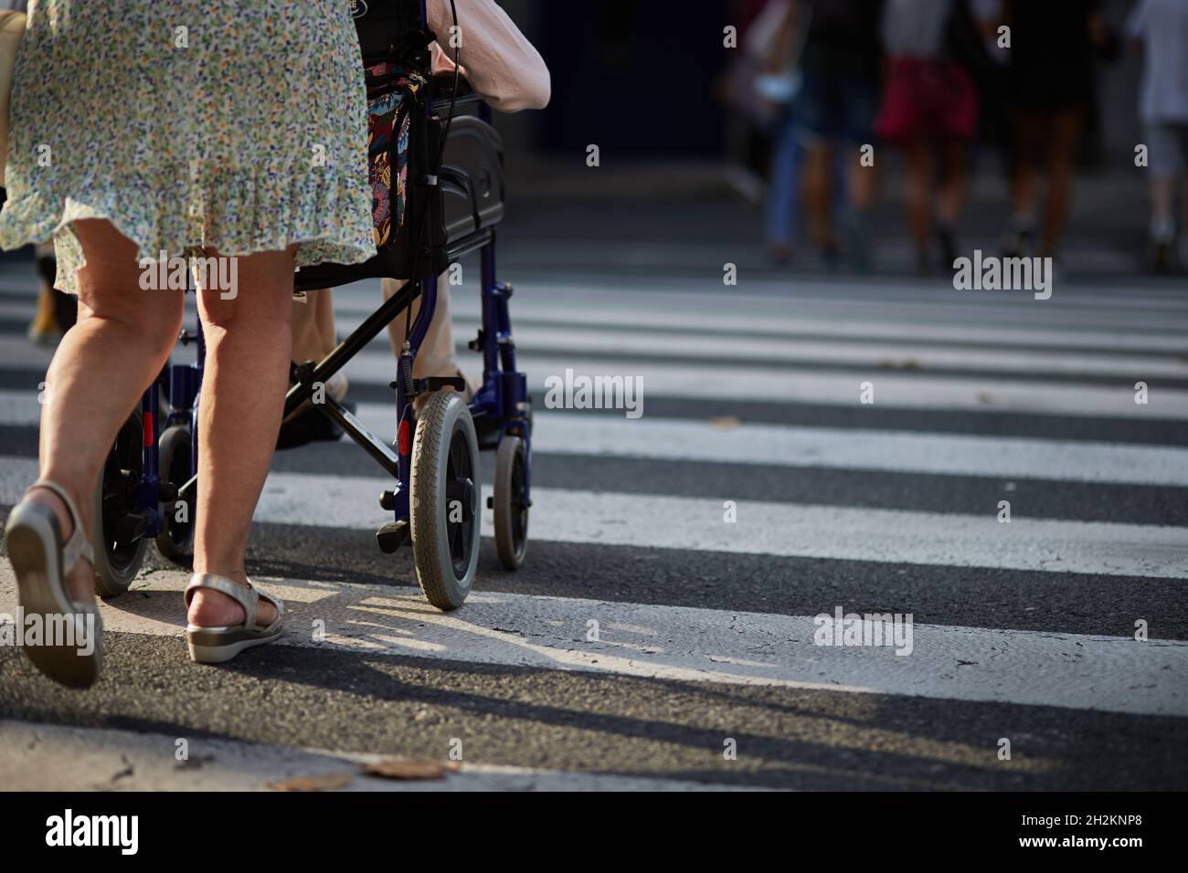 Frau hilft, die Straße zu überqueren eine Person in einem Rollstuhl. Stockfoto
