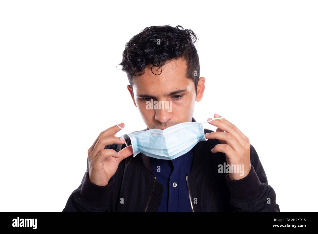 Mann, der eine Gesichtsmaske aufsetzt. Weißer Hintergrund. Junger Erwachsener, der sich vor Viren schützen will, zieht eine Gesichtsmaske an. Stockfoto