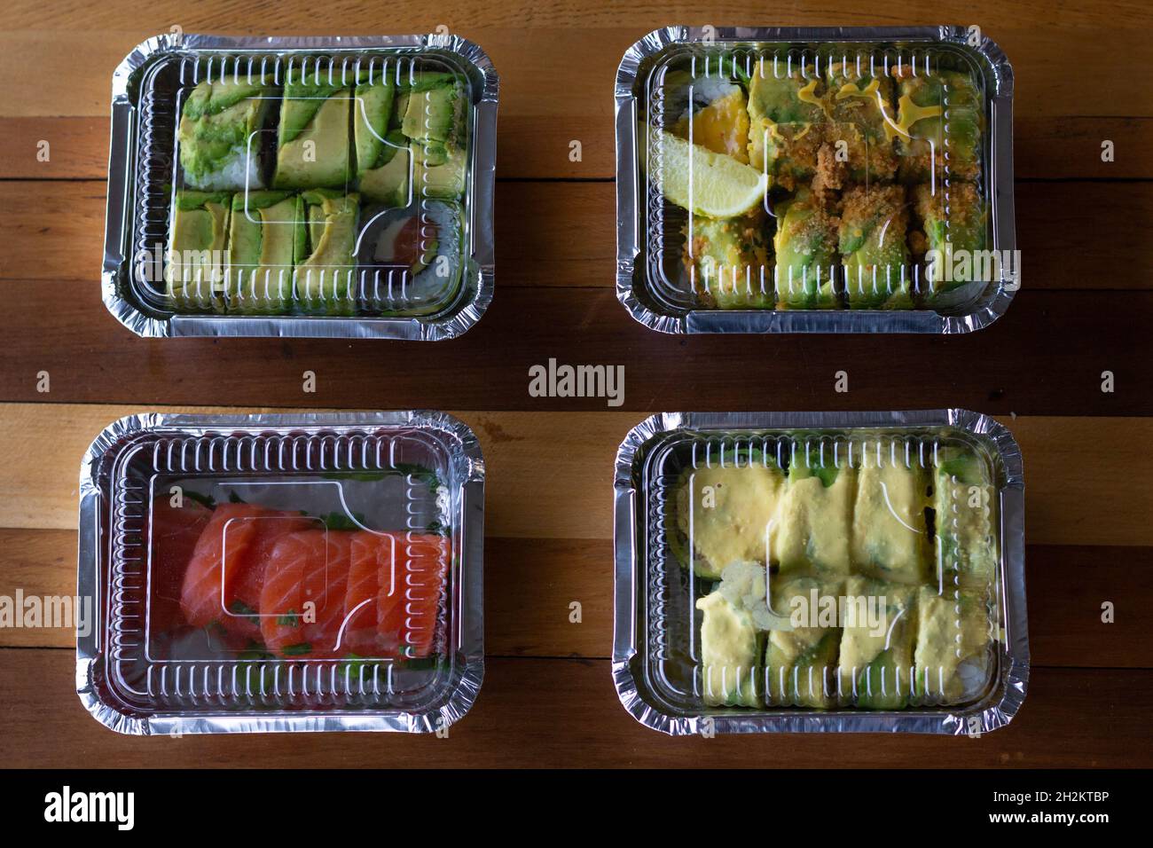 Vier Plastikboxen mit Sushi und Sashimi von oben. Konzept für die Auftragslieferung in japanischen Restaurants Stockfoto
