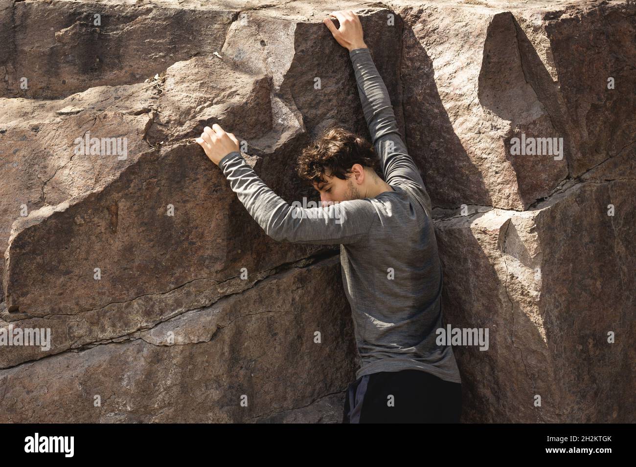 Schweißtreibender junger Mann, der an einem sonnigen, heißen Tag die Felswand klettert. Outdoor-Workout, Kampf, Erkundungskonzepte Stockfoto