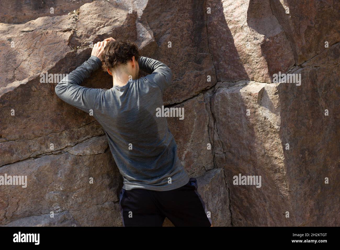 Schweißtreibender junger Mann, der sich am sonnigen, heißen Tag am Felsen festhält. Outdoor-Workout, Kampf, Erkundungskonzepte Stockfoto