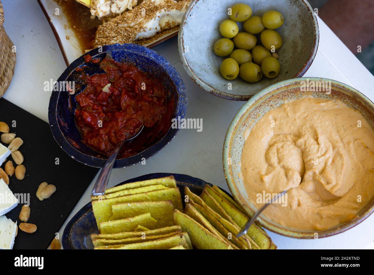 Verschiedene Schüsseln und Snackteller mit Hummus, Oliven, Crackern, Tomatensauce, Käse und Erdnüssen Stockfoto