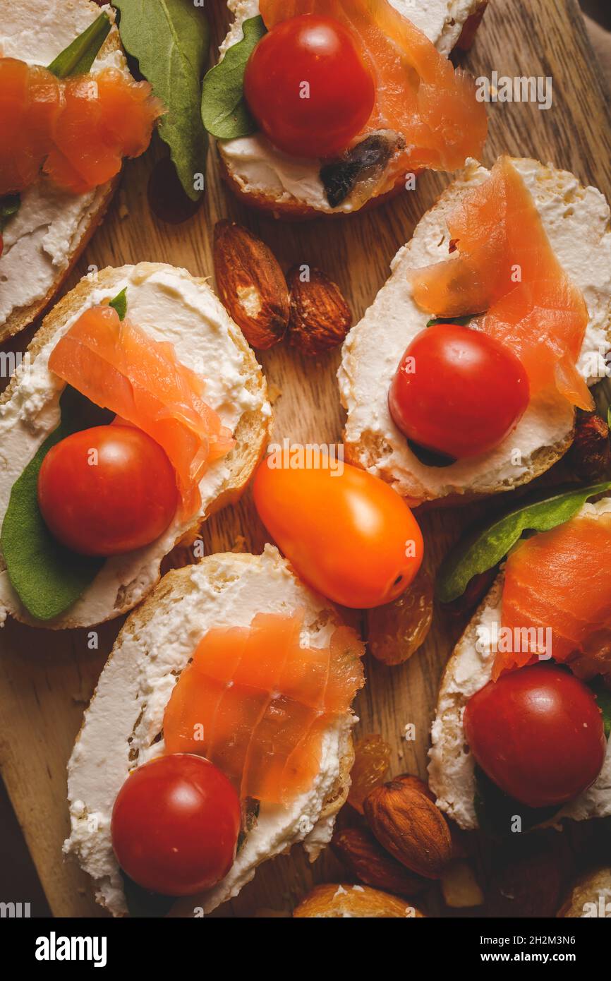 Trockener geräucherter Lachs auf den Brotscheiben und Frischkäse-Sandwiches mit Kirschtomaten und Rucola-Salat aus der Nähe von oben Stockfoto