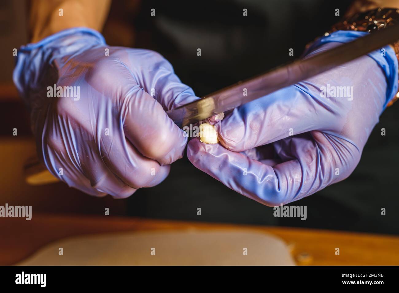 Nahaufnahme der Hände eines unbekannten Mannes oder einer unbekannten Frau, die mit einem Messer den Knoblauch schälen und schneiden Stockfoto