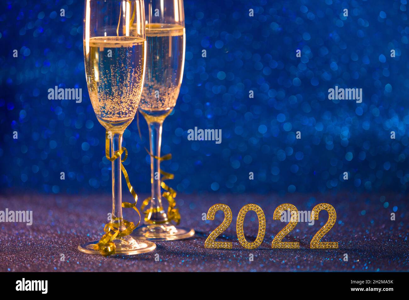 Frohes neues Jahr 2022. Weihnachten und Neujahr Hintergrund mit zwei Tassen, einem Glas Champagner und einem blauen Bokeh-Effekt Hintergrund. Stockfoto