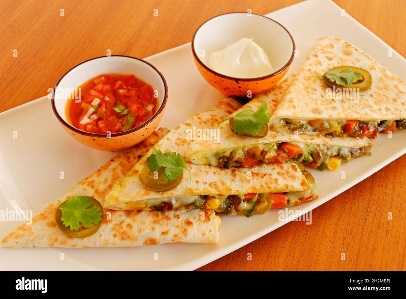 mexikanische Küche Quesadilla, würzig gekochtes Huhn und Gemüse gefüllt in Tortilla Brot mit Käse, Guacamole, Tomatensalsa und saurer Creme Stockfoto