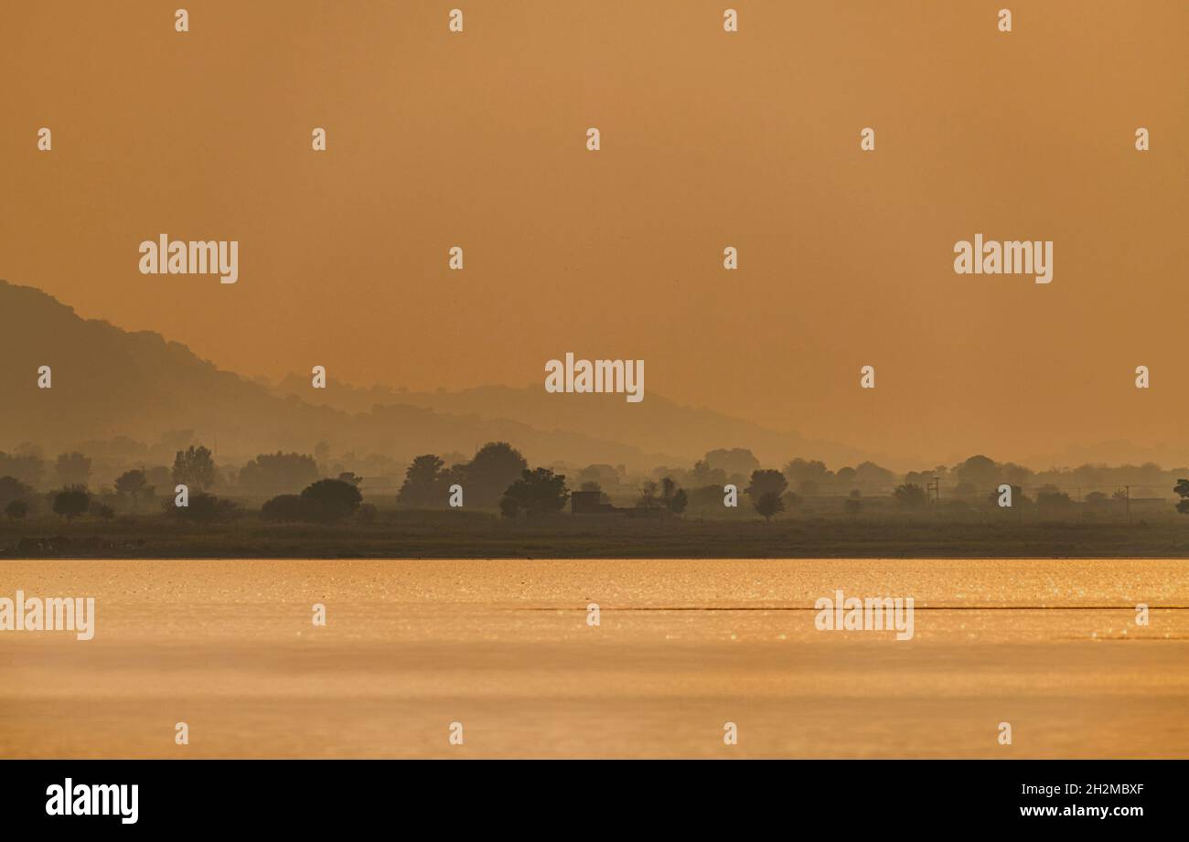 Schöne Landschaft von See und Bergen mit Bokeh von goldenem Wasser und nebligen Bergen im Hintergrund Stockfoto