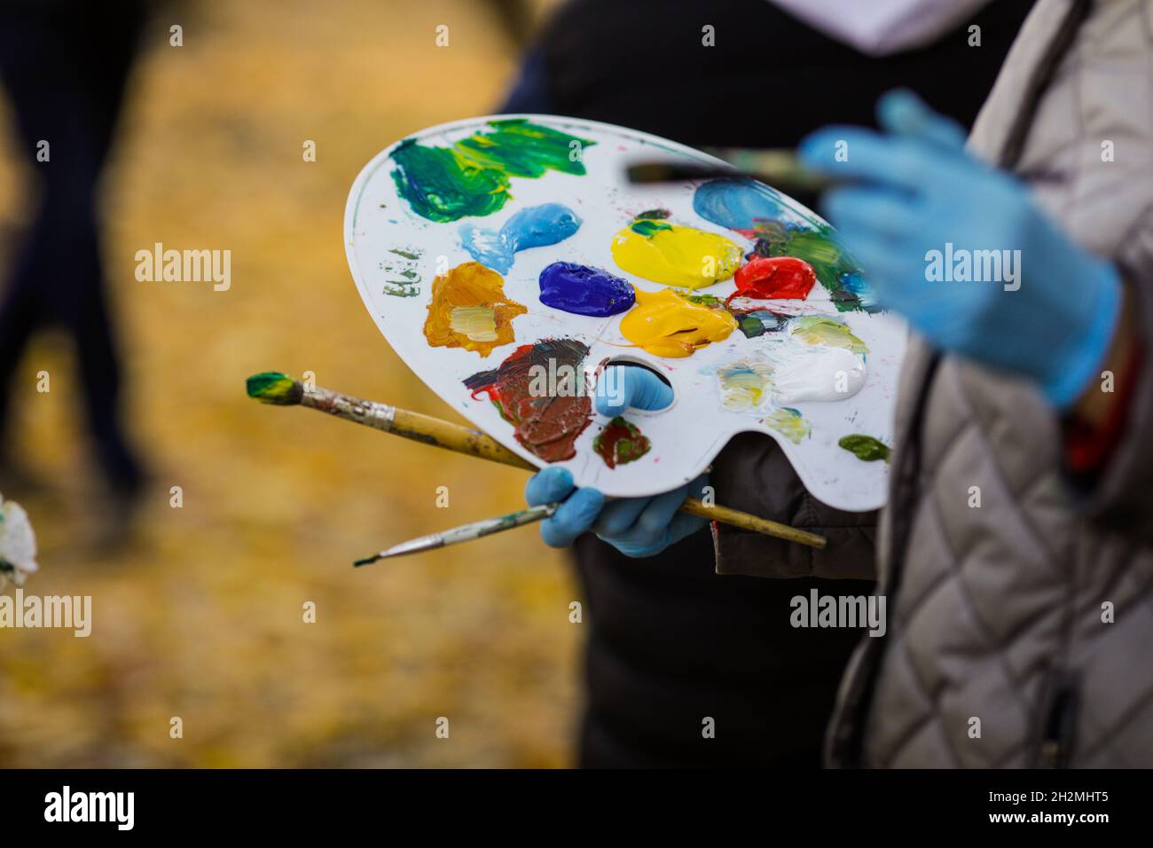 Flache Schärfentiefe (selektiver Fokus) mit der Hand einer Malerin und ihrer Farbpalette, während sie eine Landschaft auf einer sonnigen Herbstda malte Stockfoto