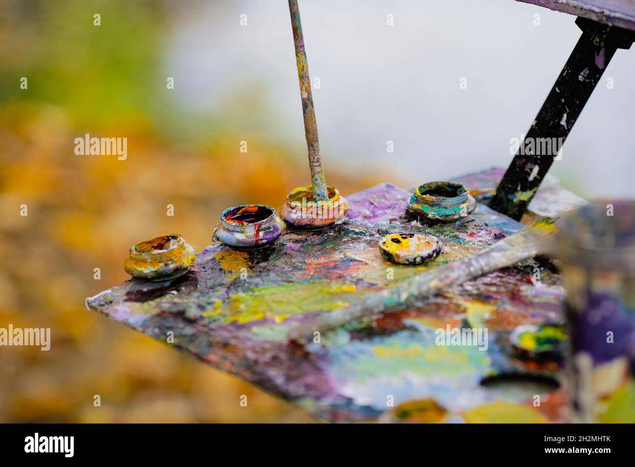 Bild mit geringer Schärfentiefe (selektiver Fokus) mit einem Maler und seiner Farbpalette, während er an einem sonnigen Herbsttag eine Landschaft malte. Stockfoto
