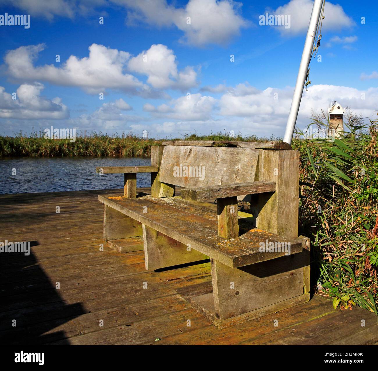 Eine rustikale Holzbank auf der Bühne am Ufer des Flusses Thurne auf den Norfolk Broads in Thurne, Norfolk, England, Vereinigtes Königreich. Stockfoto