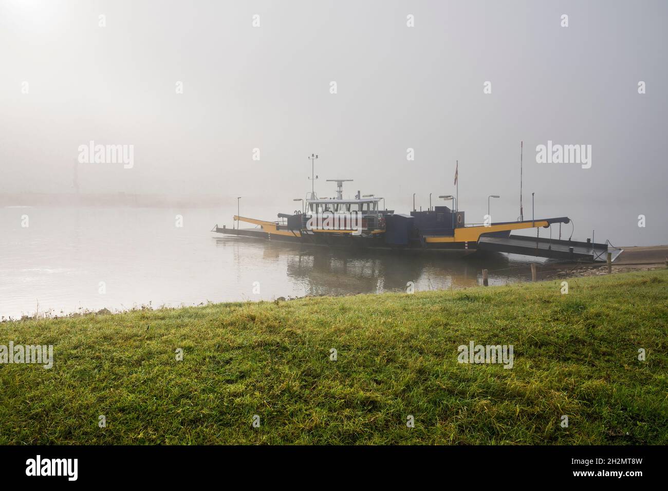 Fähre überquert den Fluss IJssel an einem nebligen Herbstmorgen bei Sonnenaufgang. Stockfoto
