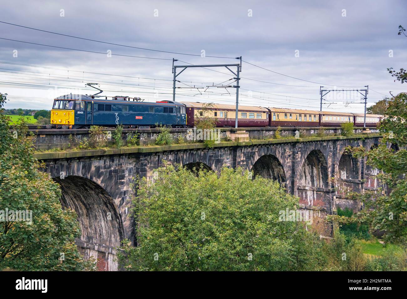 Caledonian Sleeper liveried Class 86/4, 86401 'Mons Meg', der über das Sankey Valley Viadukt in Earlestown nach Carlsile von Liverpool fährt. Stockfoto