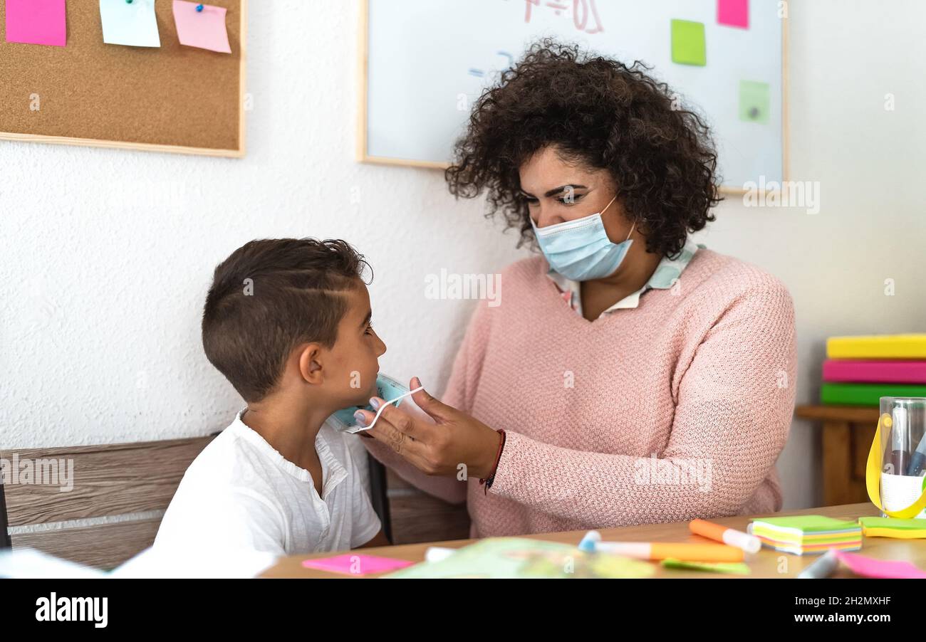 Lehrerin, die während einer Corona-Virus-Pandemie dem Schüler im Vorschulunterricht Gesichtsschutzmaske gibt - Gesundheits- und Bildungskonzept Stockfoto