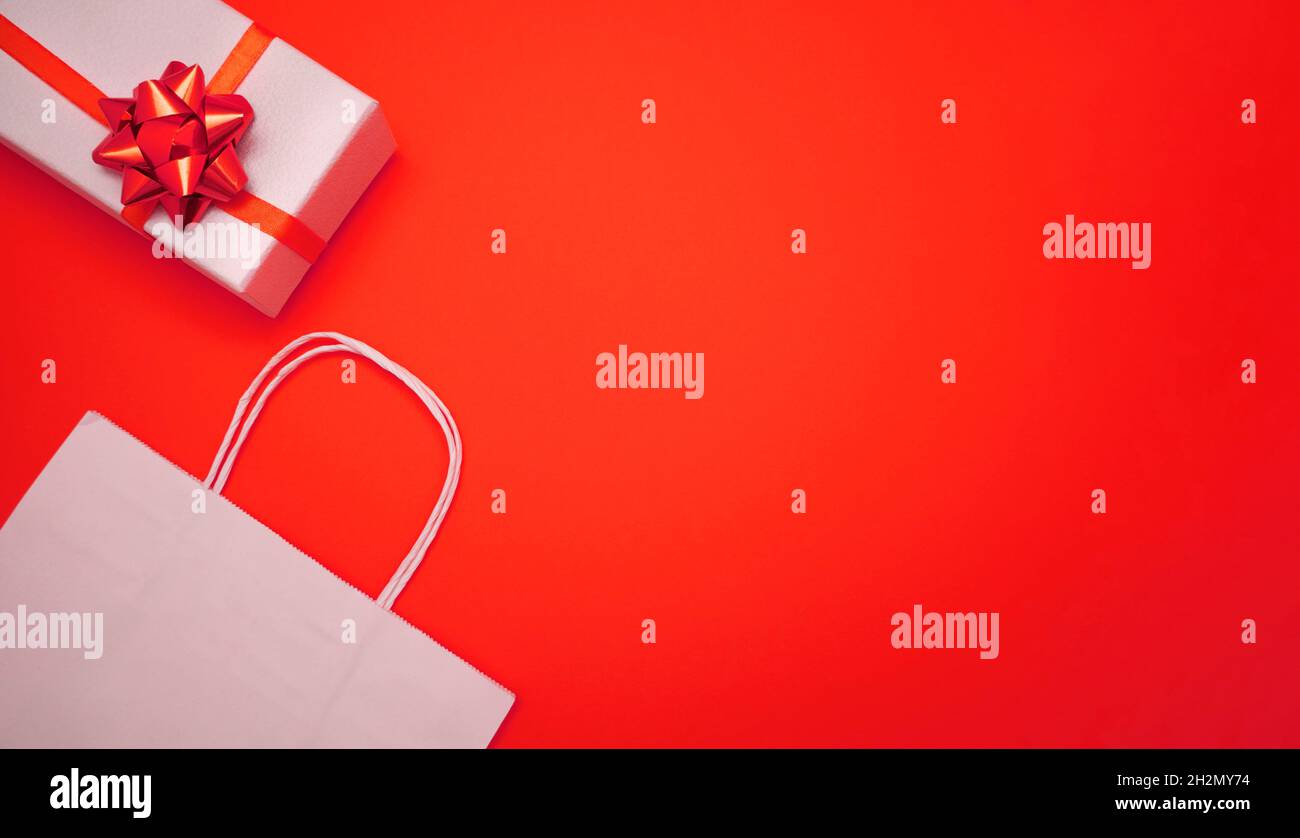Weiße Geschenkpapiertaschen und Geschenkbox auf rotem Hintergrund. Banner mit Kopierbereich. Weihnachten, Neujahr, Geburtstag, Shopping-Verkaufskonzept. Stockfoto