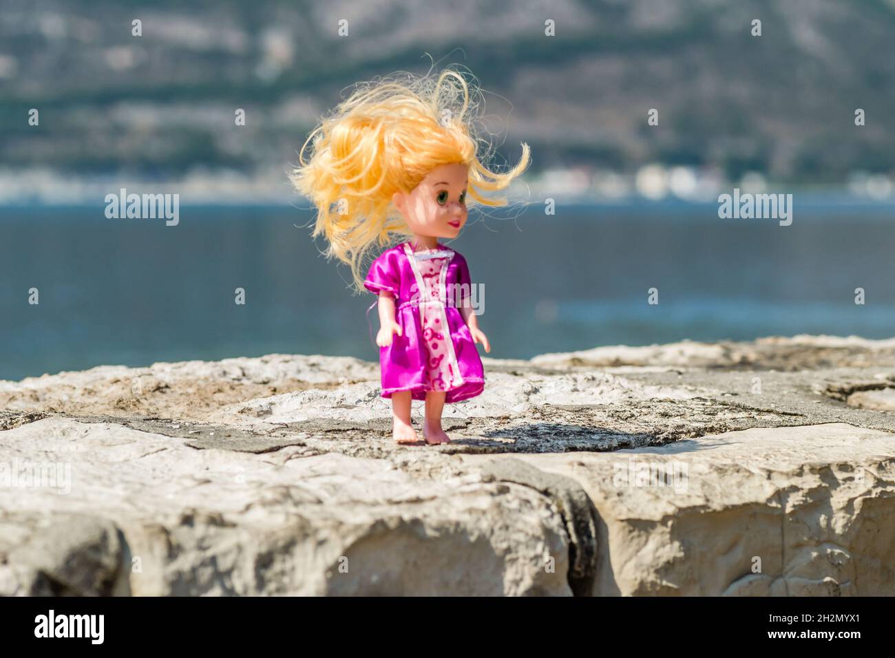 Kinderpuppe aus Kunststoff, in einem rosa Kleid, an einer Steinwand. Stockfoto