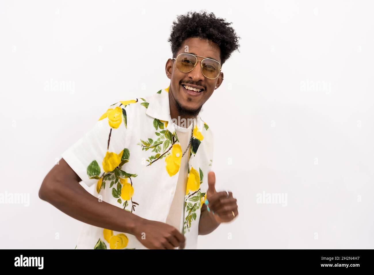Junger afroamerikanischer Mann in einem floralen Hemd, lächelnd und tanzend auf weißem Hintergrund Stockfoto