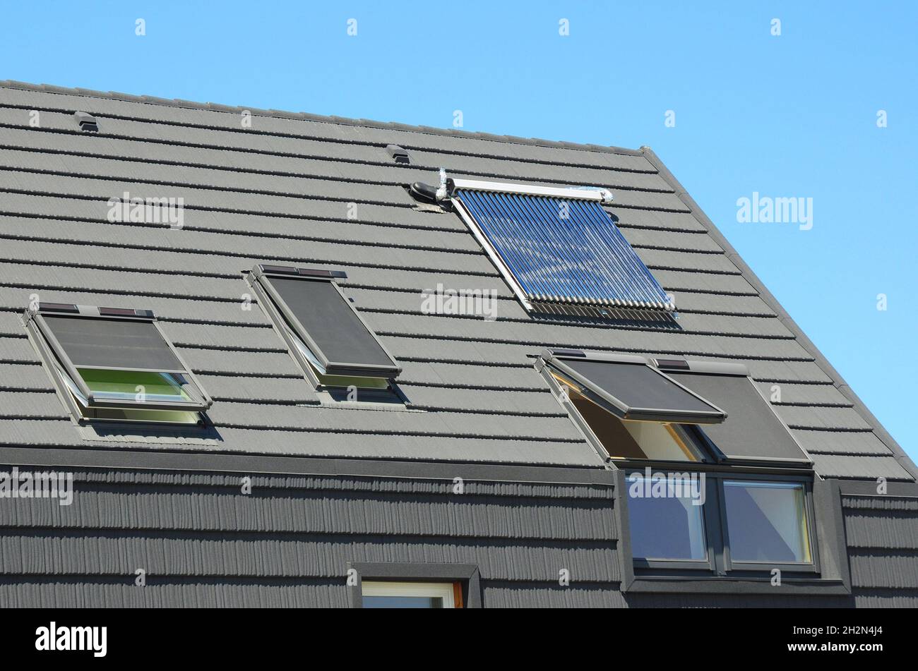 Modernes Hausdach mit Solar Water Heater, Sonnenkollektoren und Oberlichter, schönes neues zeitgenössisches Haus mit Sonnenkollektoren. Offene Dachfenster. Stockfoto