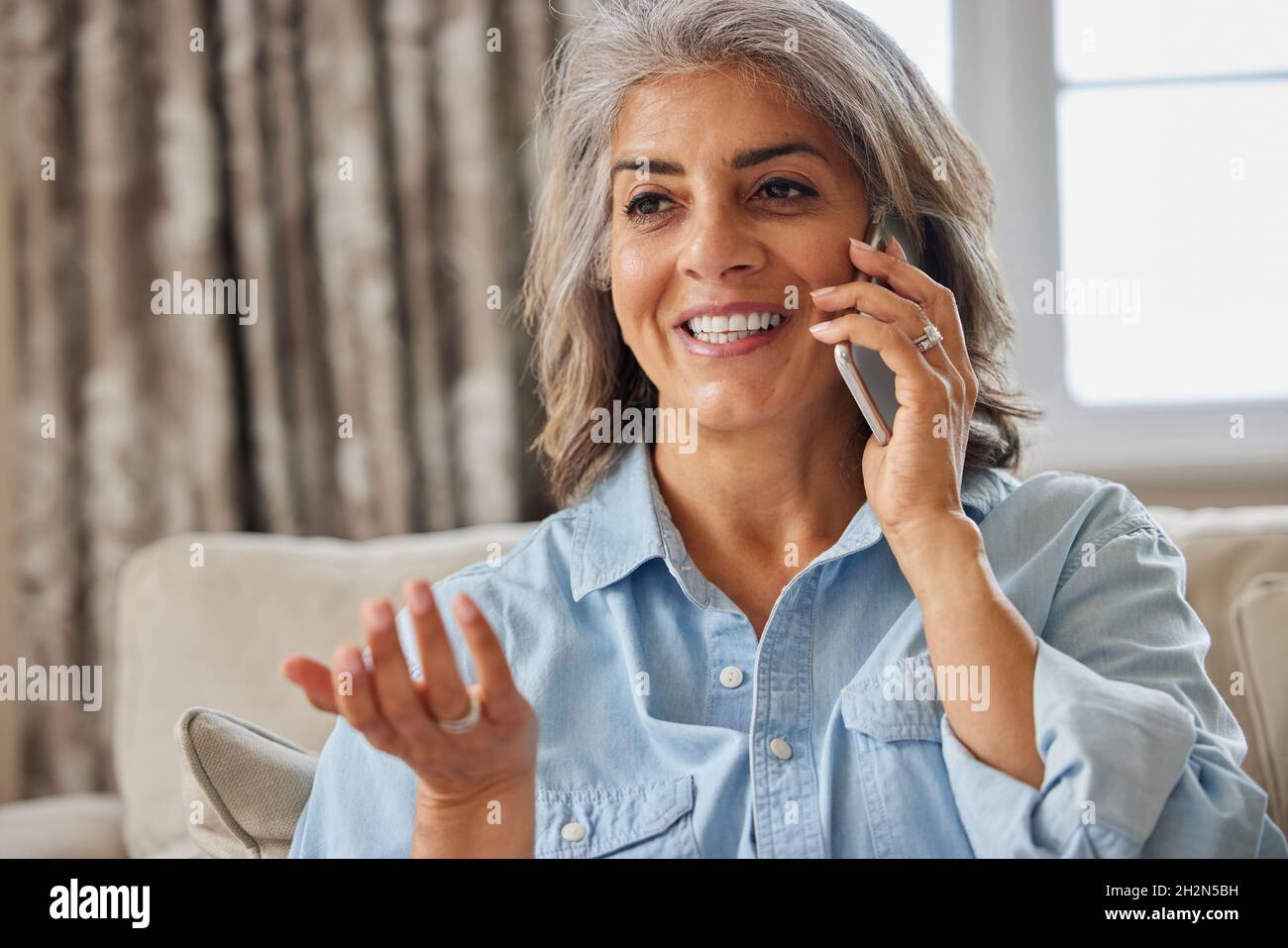 Lächelnde Reife Frau, Die Zu Hause Auf Dem Mobiltelefon Anruft Stockfoto